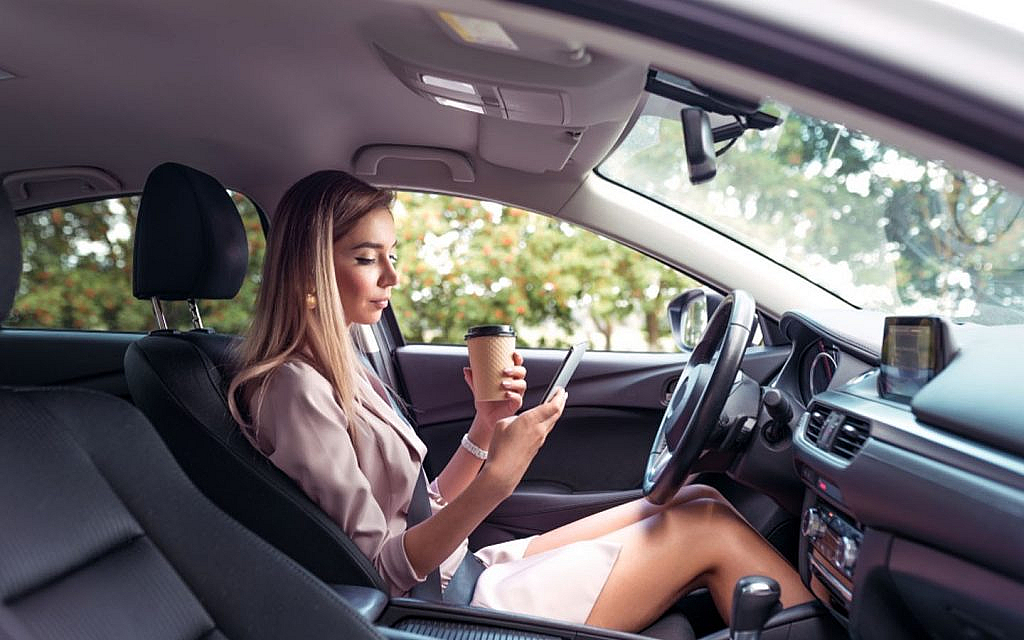 a girl is eating and using a phone while driving a car