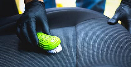 A man cleaning stains from a car’s seat with a brush