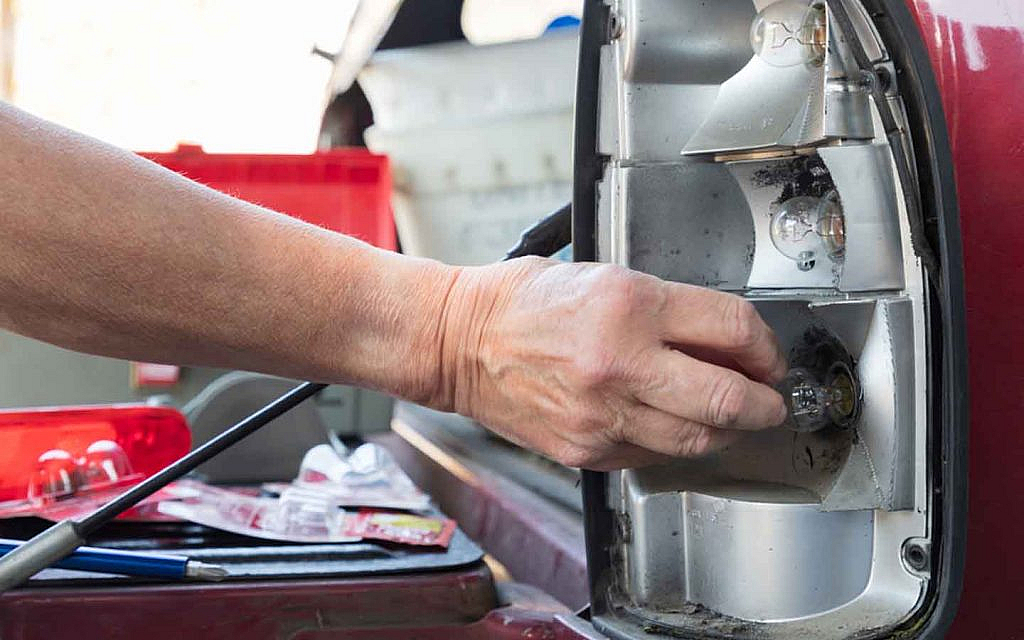 A man replacing a light bulb in the tail light assembly of a car 