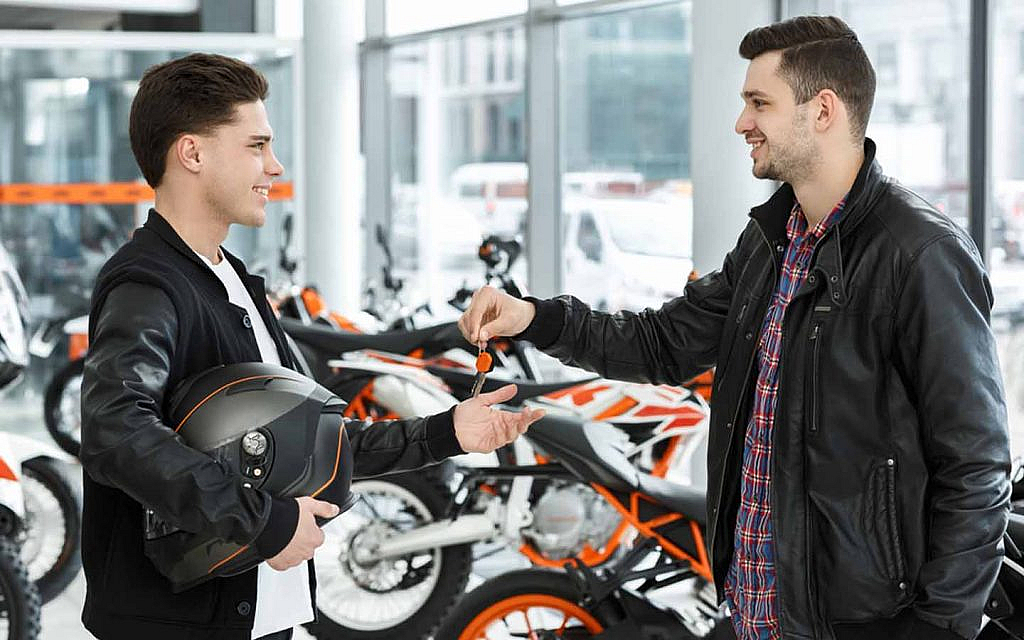 A man handing over motorbike keys to another man carrying a helmet 