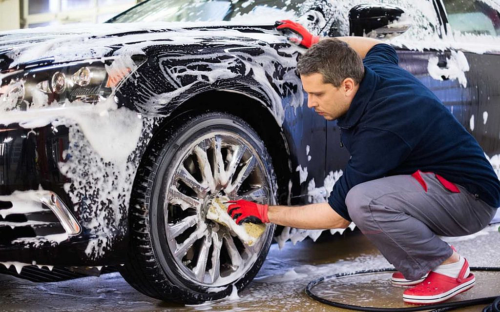 A worker washing the wheels of a car