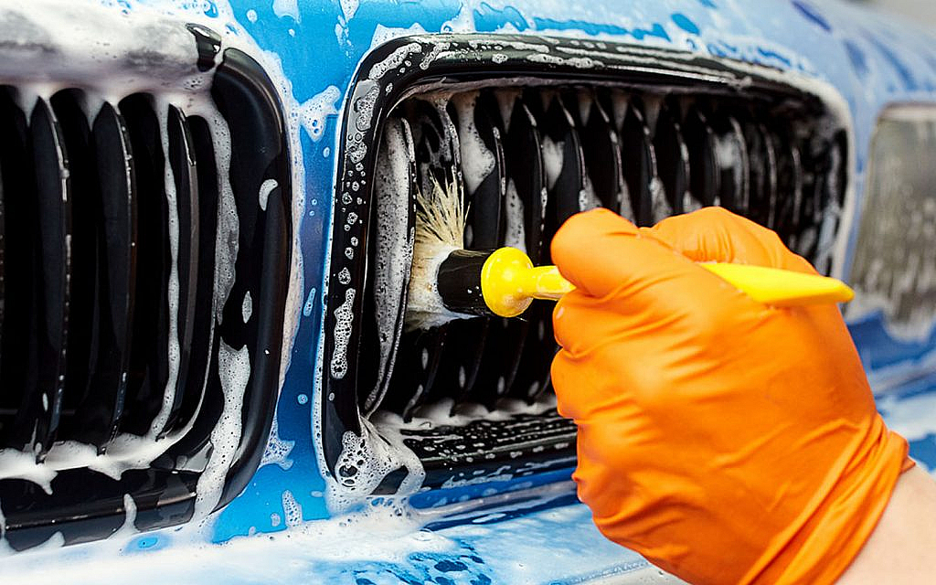 A blue car being cleaned with a brush 