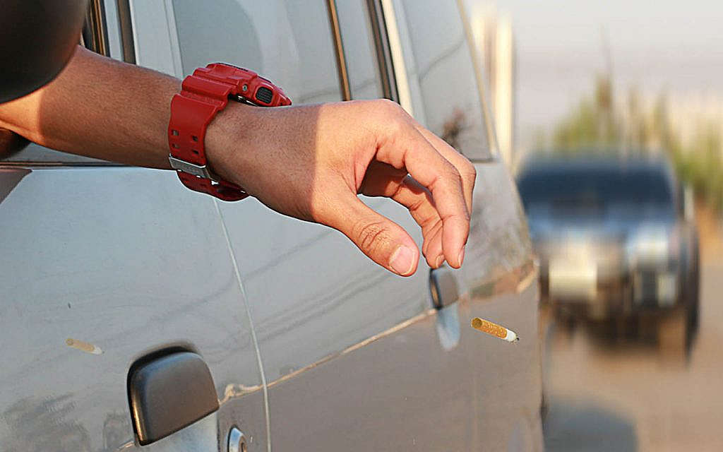 A person throwing a cigarette butt out of the window
