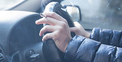 Smoking is bad for cars. Man smoking in a car with windows rolled down for ventilation.