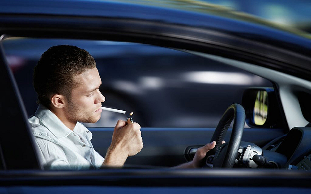 Young man lighting up a cigarette in his car