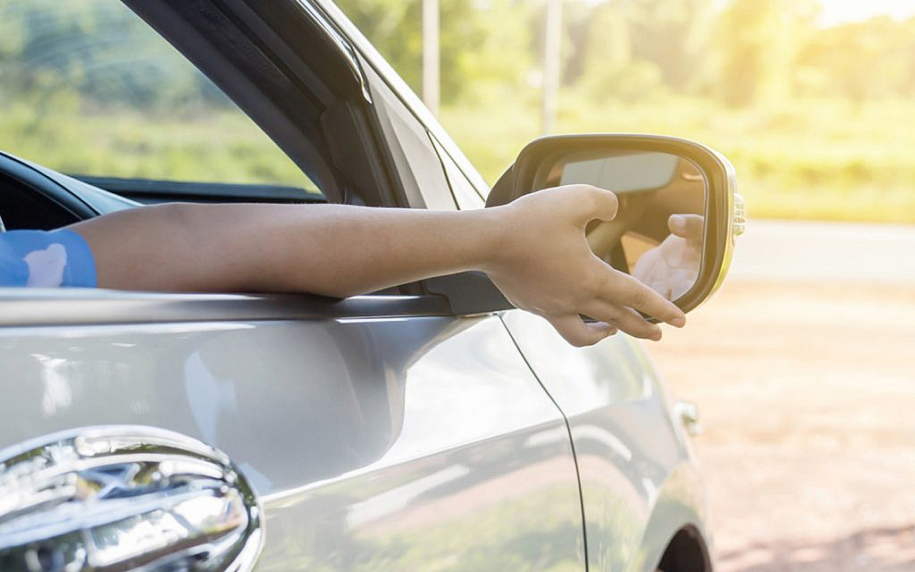 driver adjusting car's side mirror