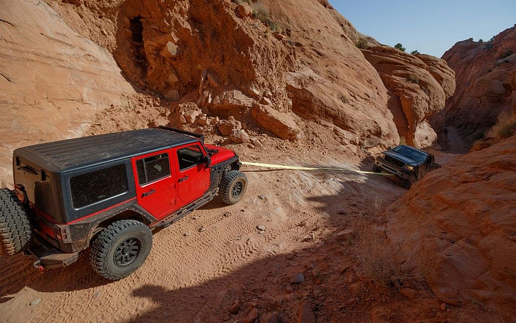 Vehicle being pulled out of a rocky terrain using a recovery strap 