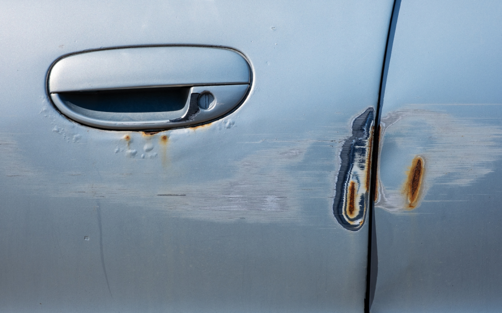 A silver car with smaller dents and rust