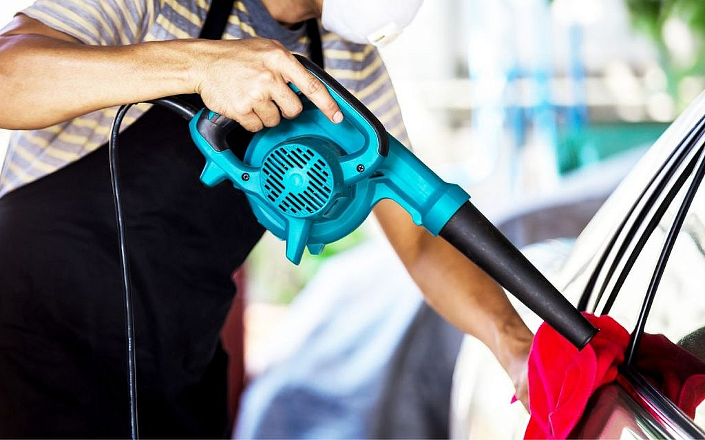 Man using a red blower on a car