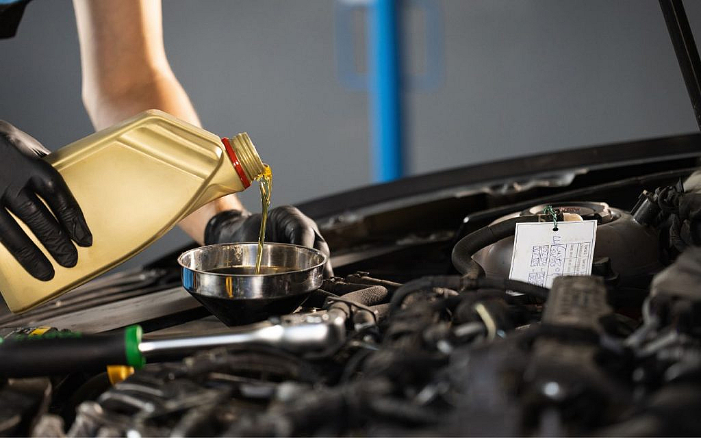 The mechanic is adding oil to the car's engine.
