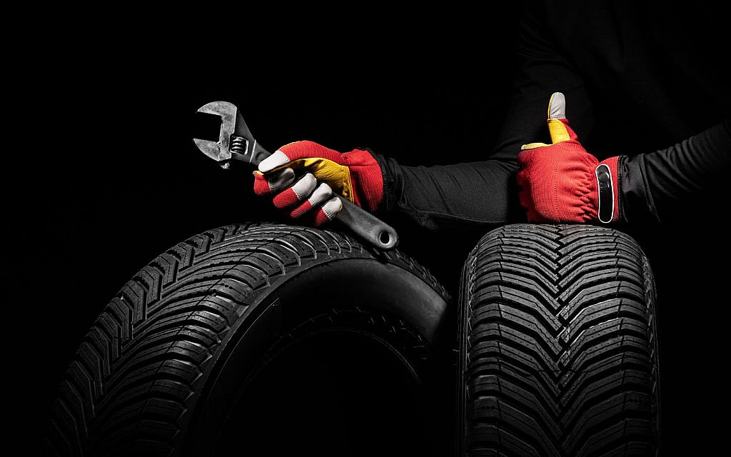 A mechanic holds two tires and a wrench, giving a confident thumbs-up.