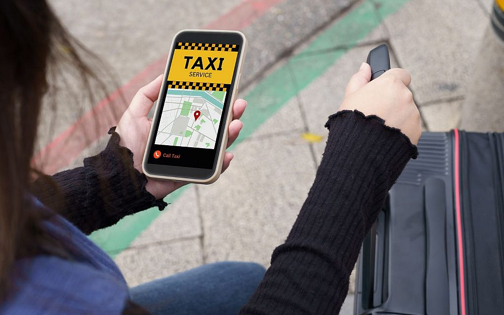A woman standing on a city street using her smartphone to book a taxi