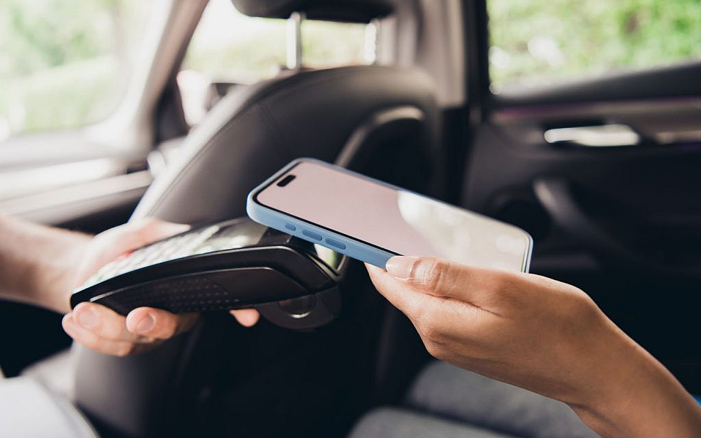 A woman making a payment with her smartphone inside a taxi.