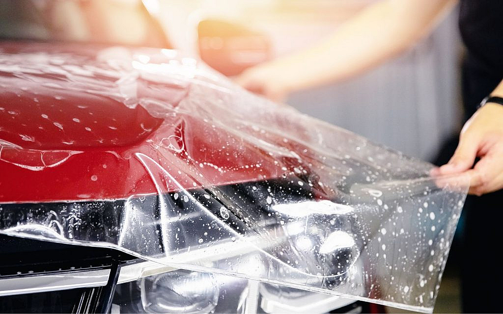 Applying protective wrap on red car hood