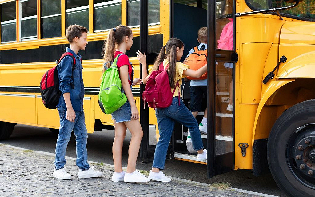 Children happily boarding a school bus in the UAE, guided by a supervisor.
