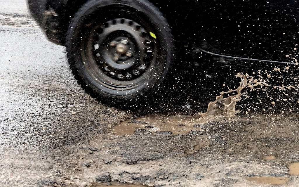A car driving through a water-filled pothole, risking off-centre steering issues.