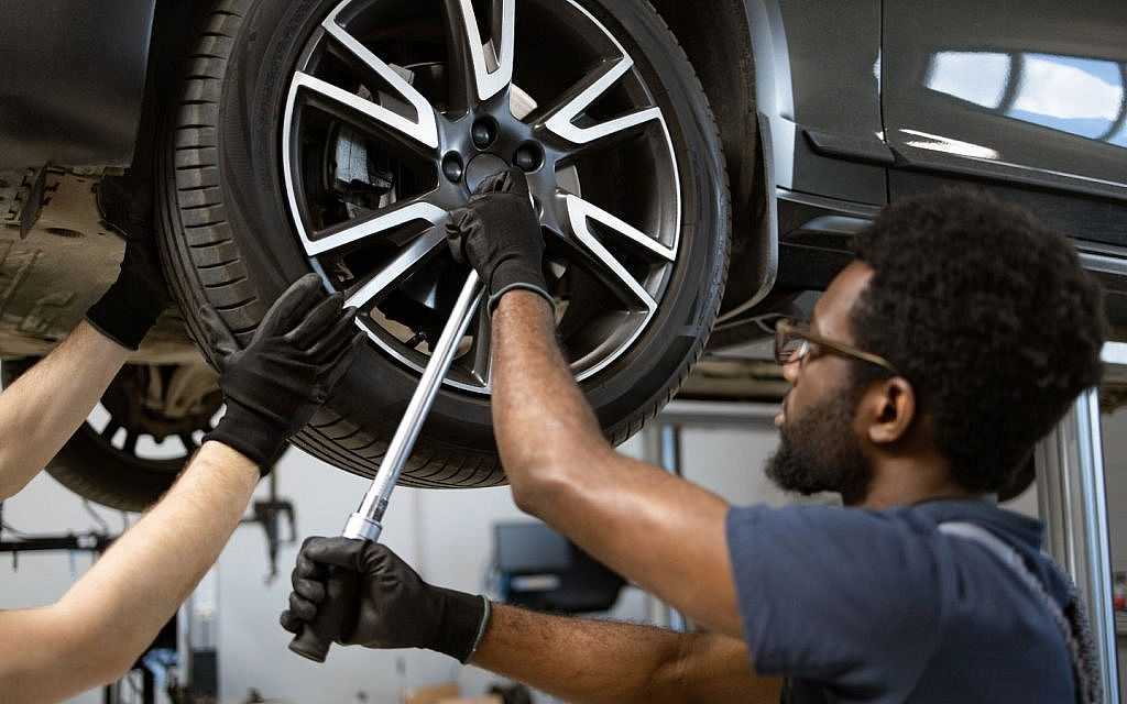 A car wheel being repaired by two mechanics to correct off-centre steering.