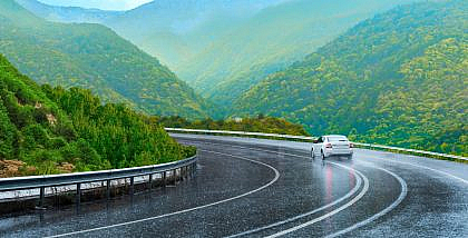 Car driving through rain on a scenic road with greenery – What to pack for a rainy road trip.