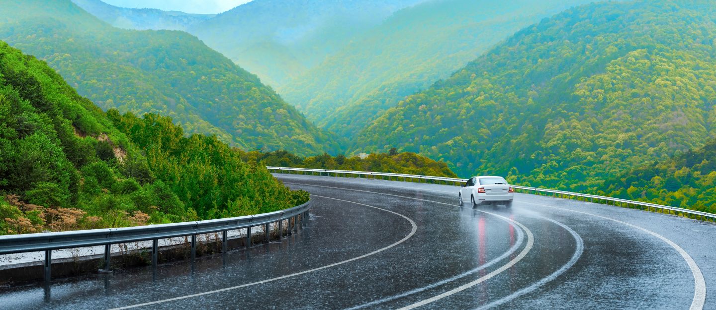 Car driving through rain on a scenic road with greenery – What to pack for a rainy road trip.