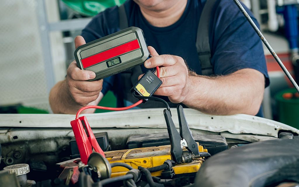 A man is using a portable jump starter to charge a car battery.