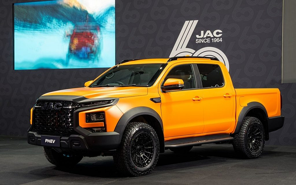An orange JAC T9 Hunter pickup truck is displayed indoors in front of a screen and a JAC logo.