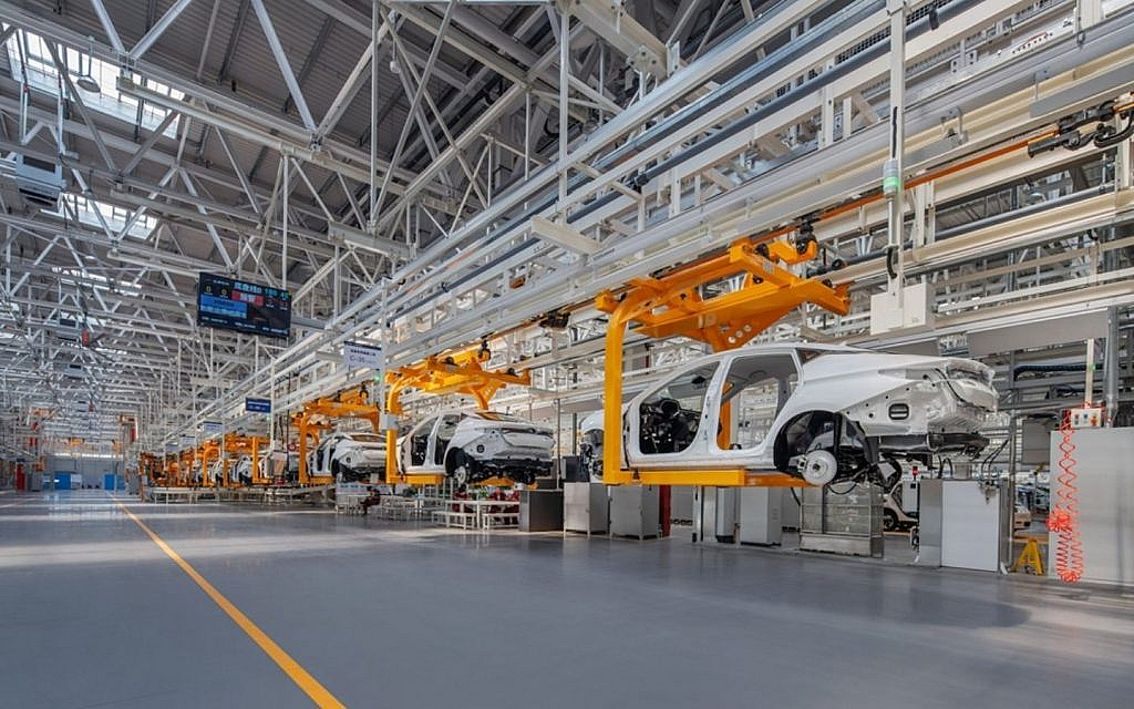 An automotive assembly line with several white car bodies being moved by overhead machinery.