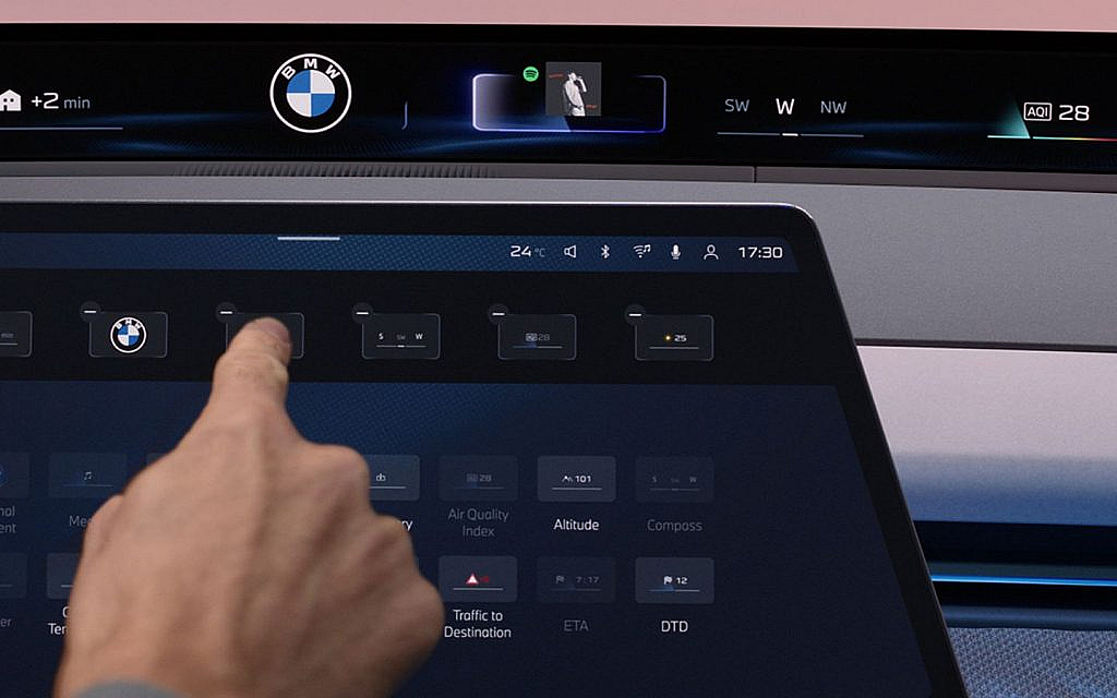 A human hand is gently touching the sleek Panoramic iDrive display, interacting with its intuitive controls.

