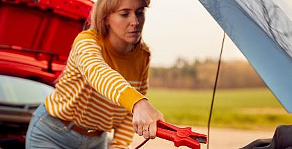Woman attaching jumper cables to a car battery, illustrating how long to run a car after jump-starting.