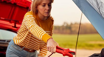 Woman attaching jumper cables to a car battery, illustrating how long to run a car after jump-starting.