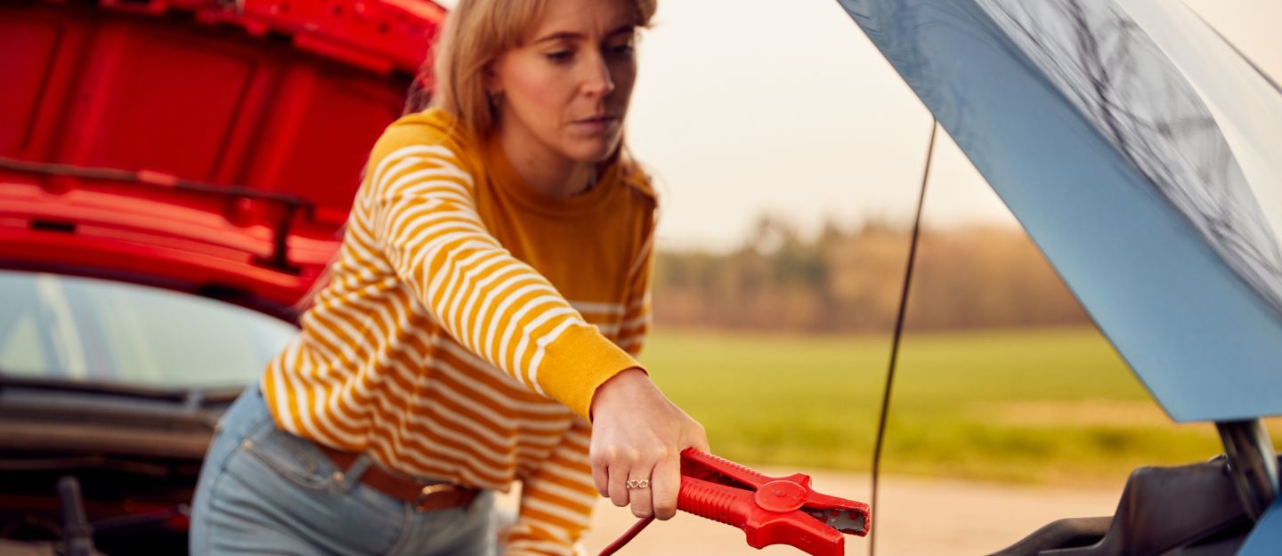 Woman attaching jumper cables to a car battery, illustrating how long to run a car after jump-starting.