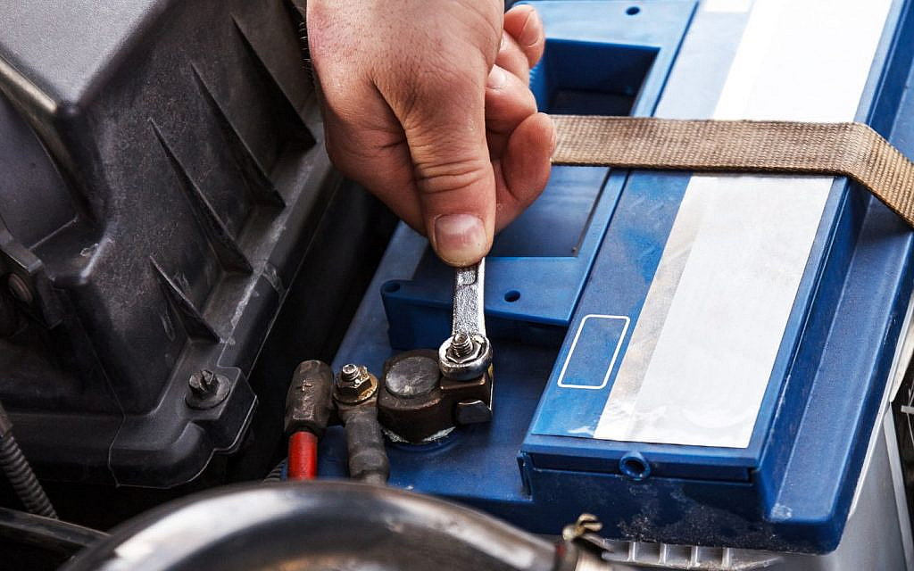 A mechanic is installing a new car battery in a vehicle at a garage.