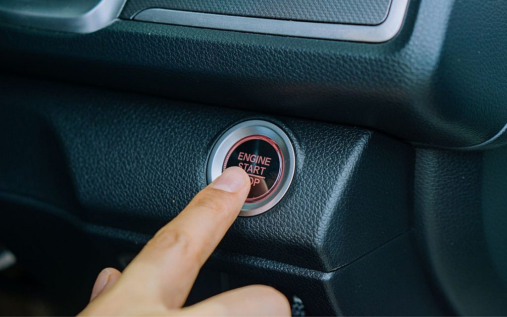 Close-up of a finger pressing a car’s start/stop button to start the engine.