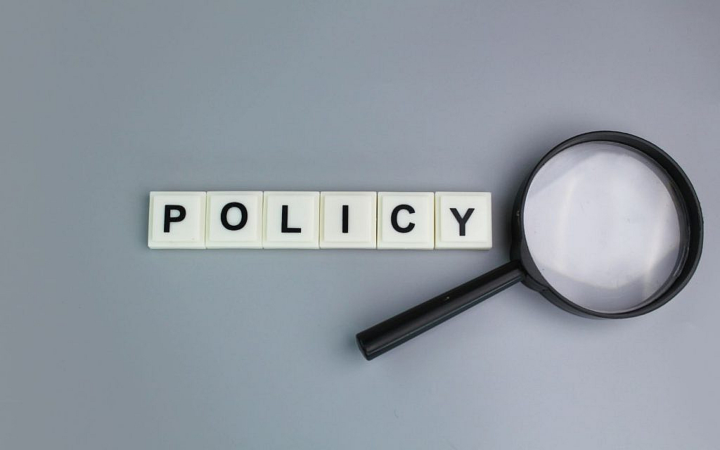 A grey colour background with a magnifying glass and an alphabet of policy.