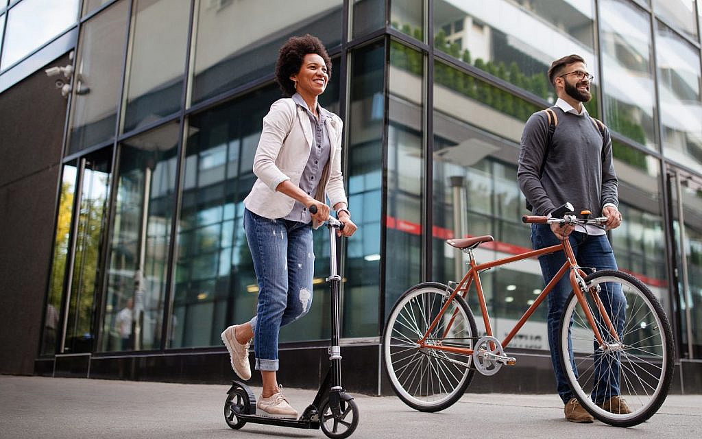 Happy business people riding an electric scooter and a bicycle to work on a city street in Dubai. 