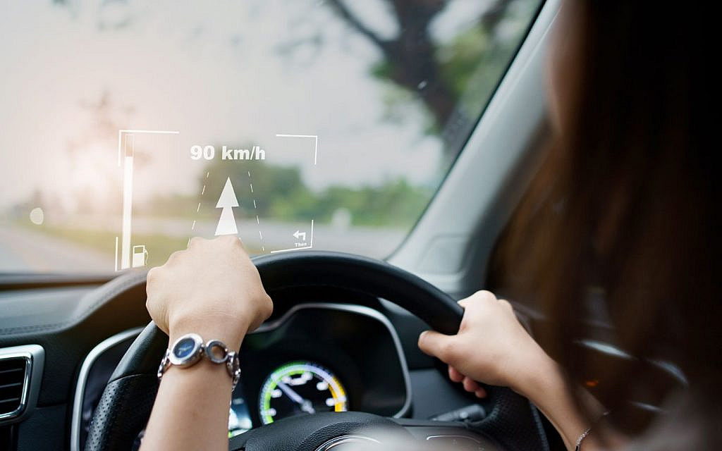  A woman driving a modern electric vehicle, hands on the steering wheel, with a digital dashboard visible.
