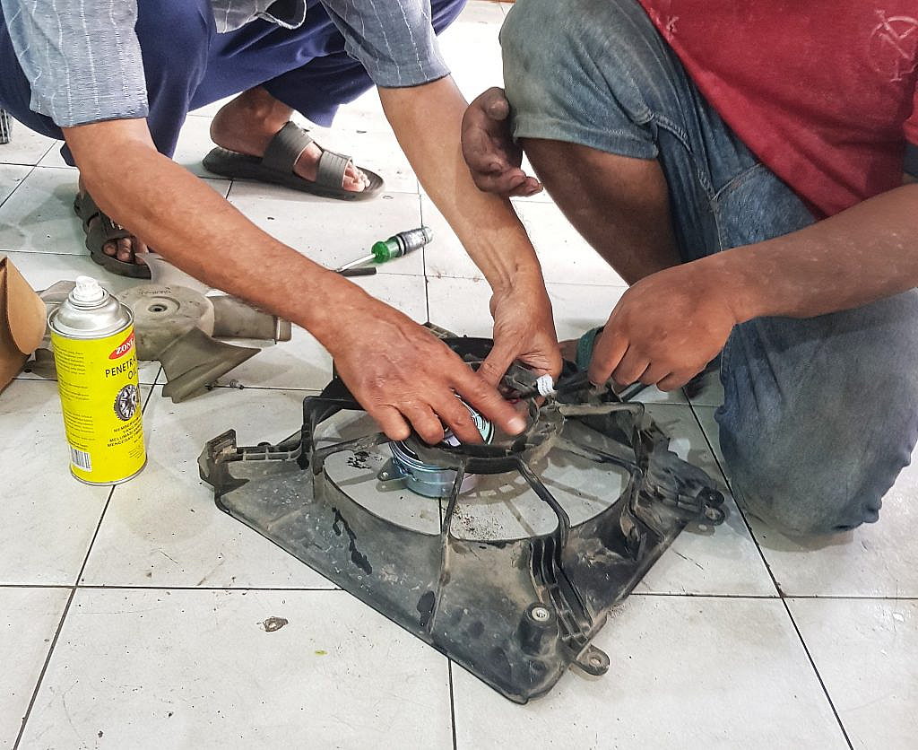 شخصان يصلحان مروحة تبريد سيارة