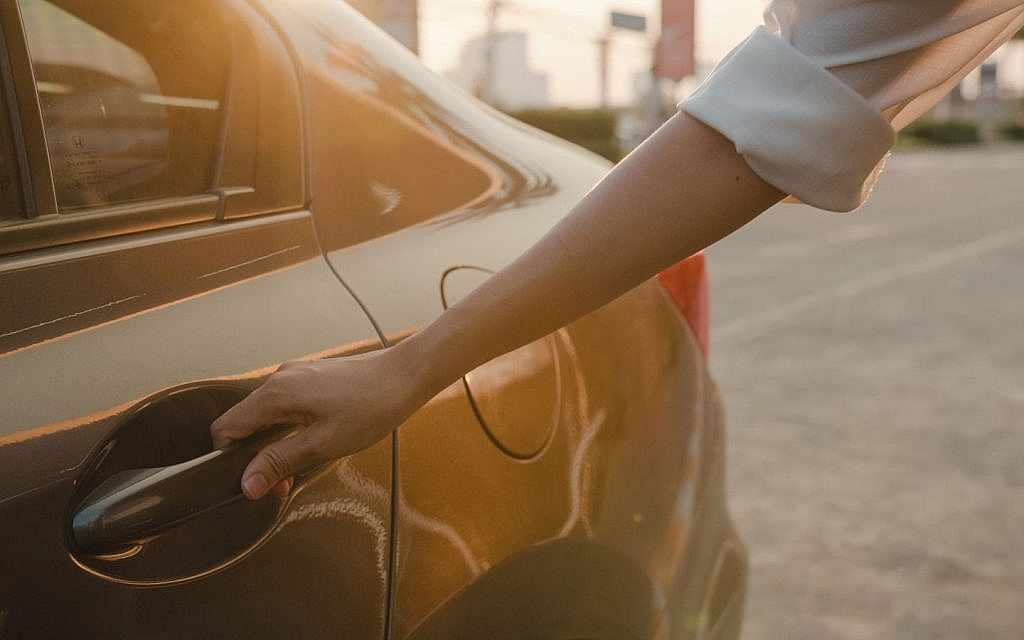 A woman’s hand opening the rear door of a parked car.