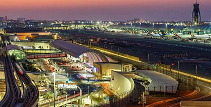 Dubai International Airport at night with lit signage, parked planes, taxis, and people — travel from Dubai Airport to Sharjah