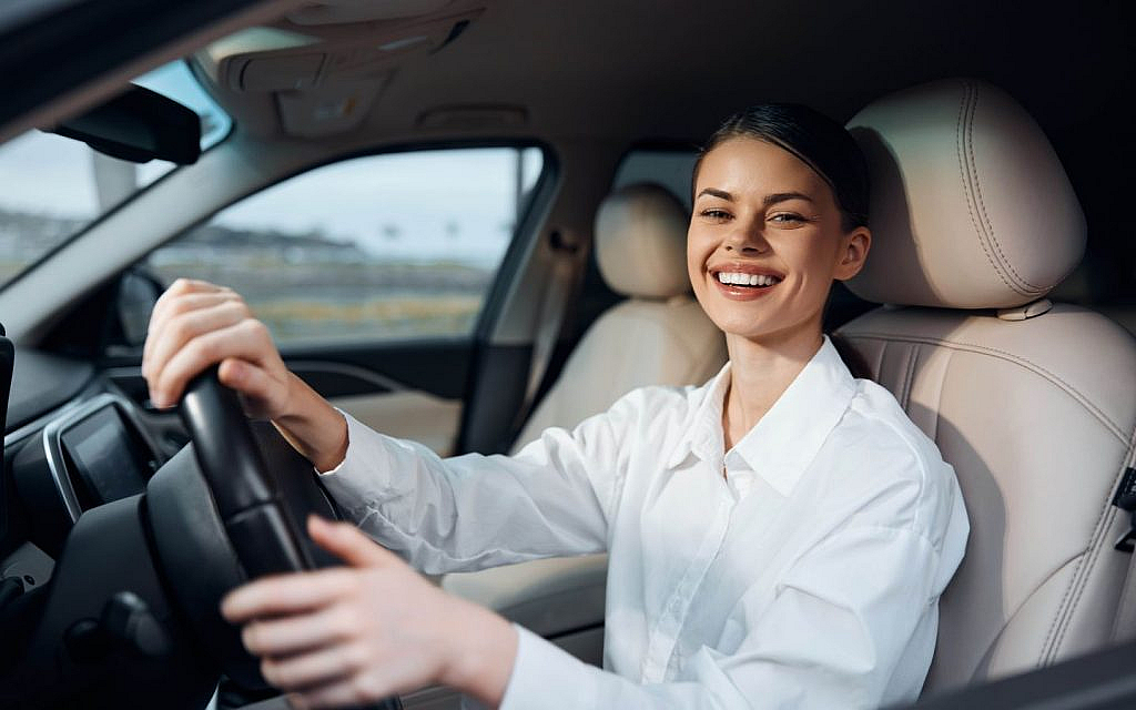 A smiling woman in a car using an automated parking system with her hands off the steering wheel 