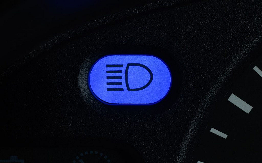 A Close-up of a car dashboard showing the illuminated high beam indicator light. 