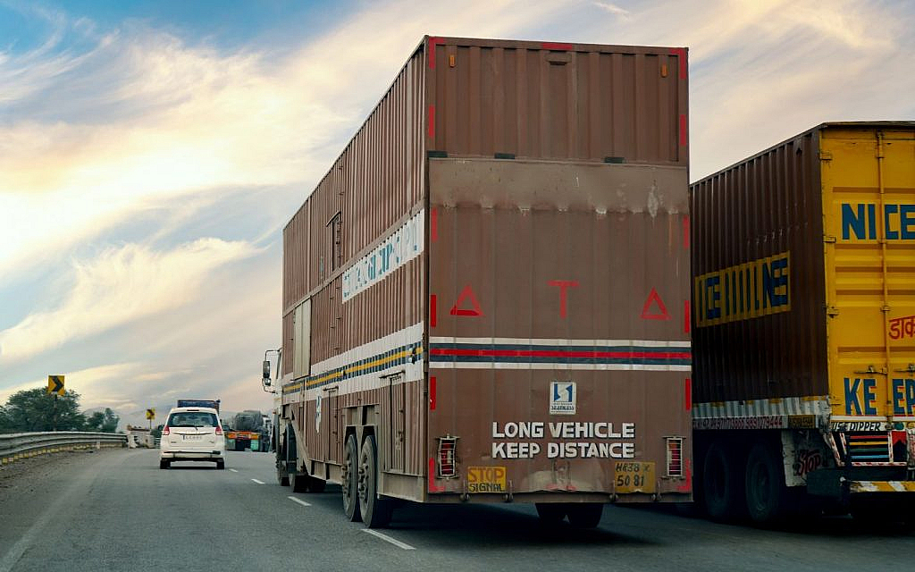 Highway scene with two trucks, one overtaking and a white car in left leftmost lane.