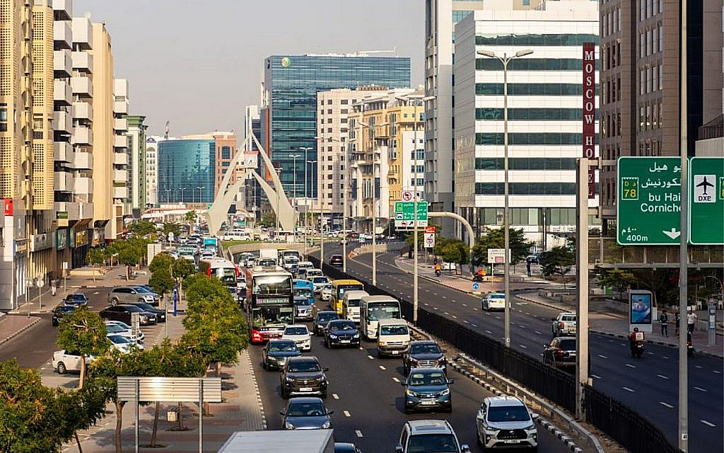 A busy multi-lane road in a city with cars, buses and tall buildings under a clear sky.
