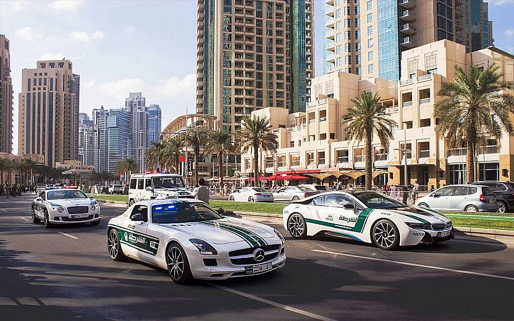 Dubai Police luxury patrol cars on a city street with skyscrapers and palm trees.
