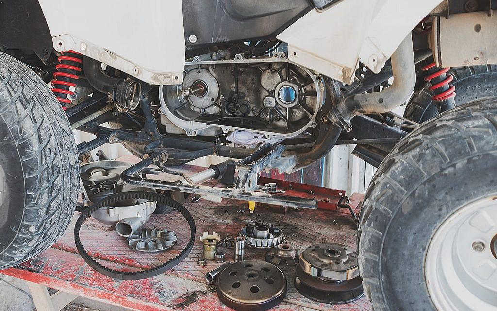 Close-up of an ATV's exposed engine and transmission with various parts.