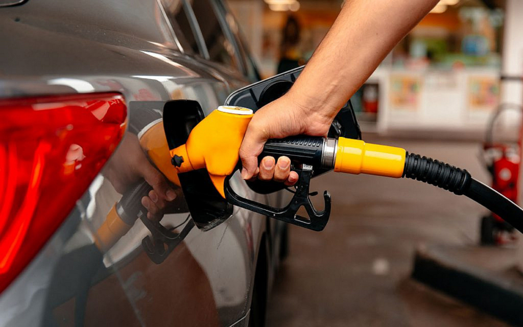 Hand holding a yellow and black fuel nozzle, refuelling a car at a gas station.
