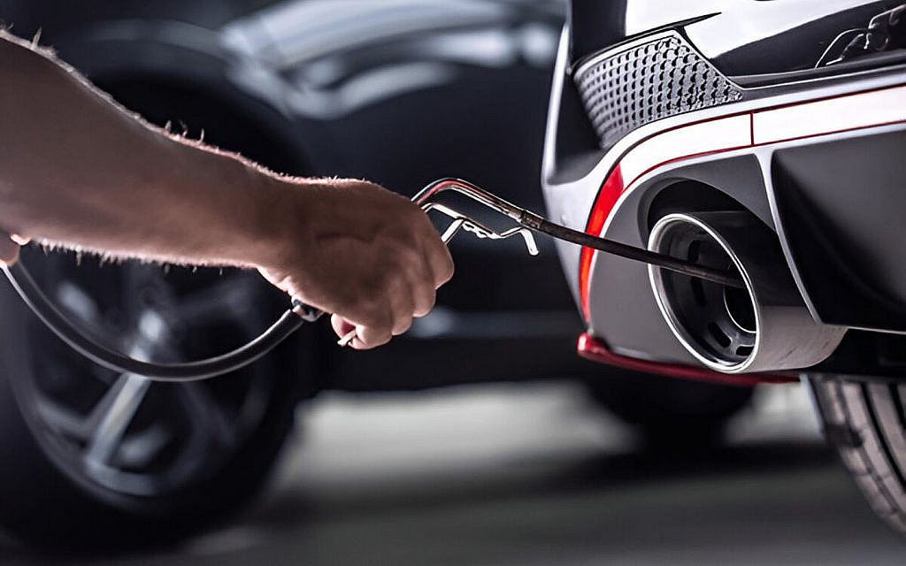 A mechanic cleaning the exhaust pipe of a black sedan