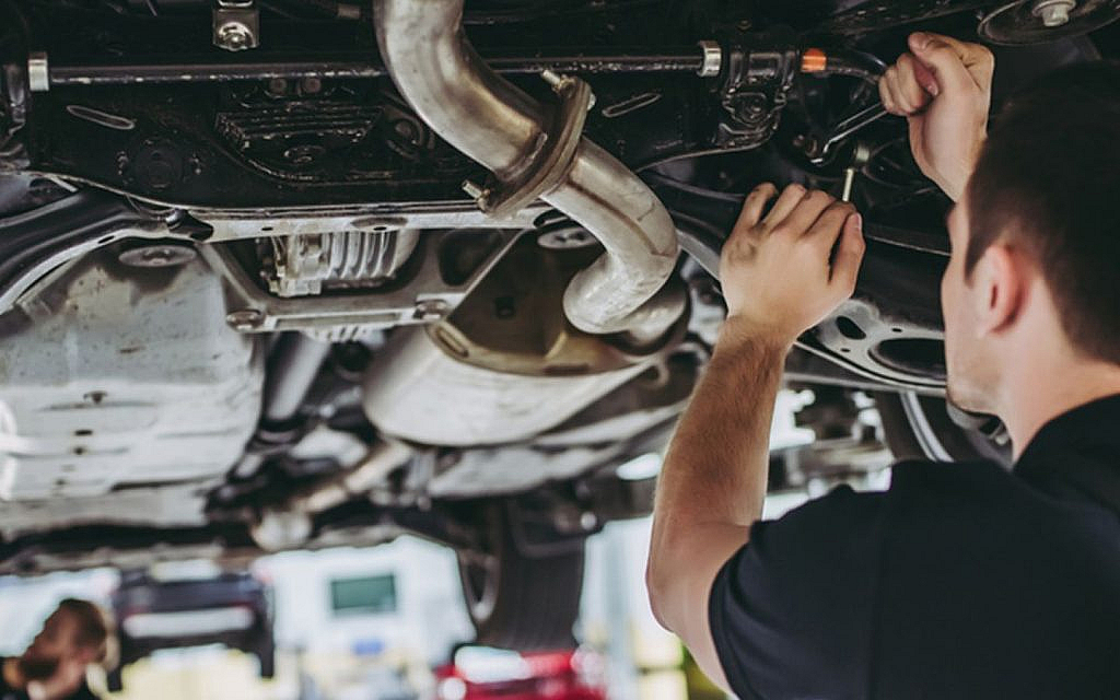  A mechanic's hands working on the undercarriage of a car on a lift.
