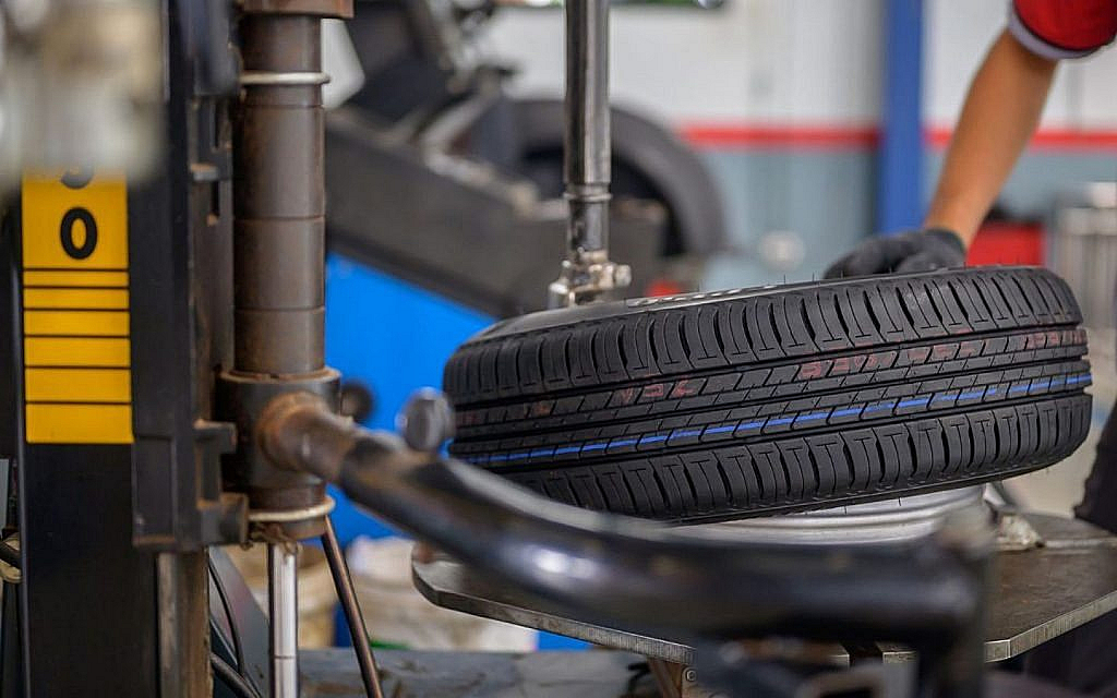 Close-up of a new tyre being mounted onto a rim using a tyre changing machine, with a gloved hand visible.