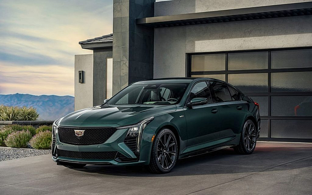 A dark green Cadillac CT5 sedan is parked in a driveway in front of a garage with a mountain view.