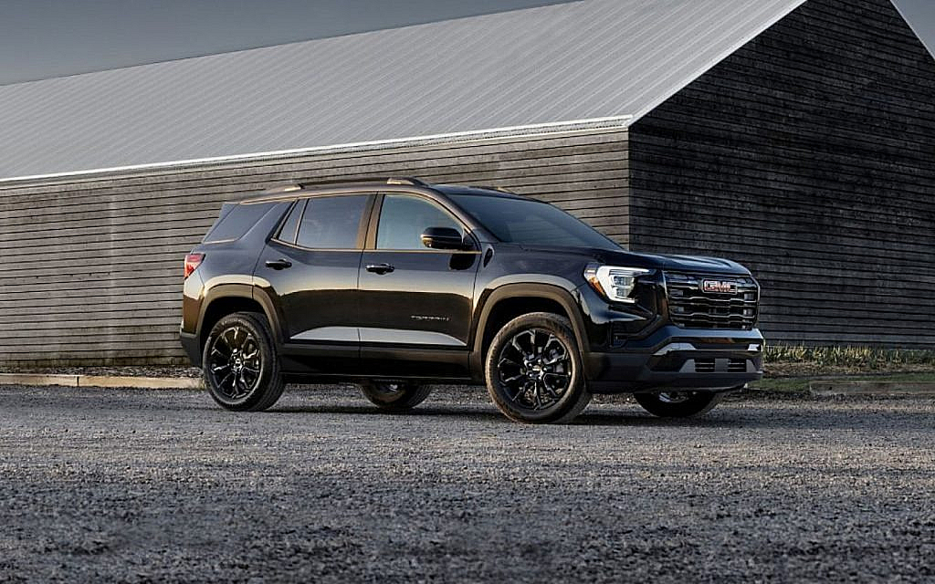 A black GMC Terrain AT4 SUV is parked on a gravel lot in front of a wooden and metal building.